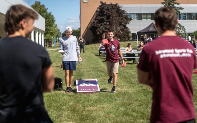 Four students playing cornhole outside on campus